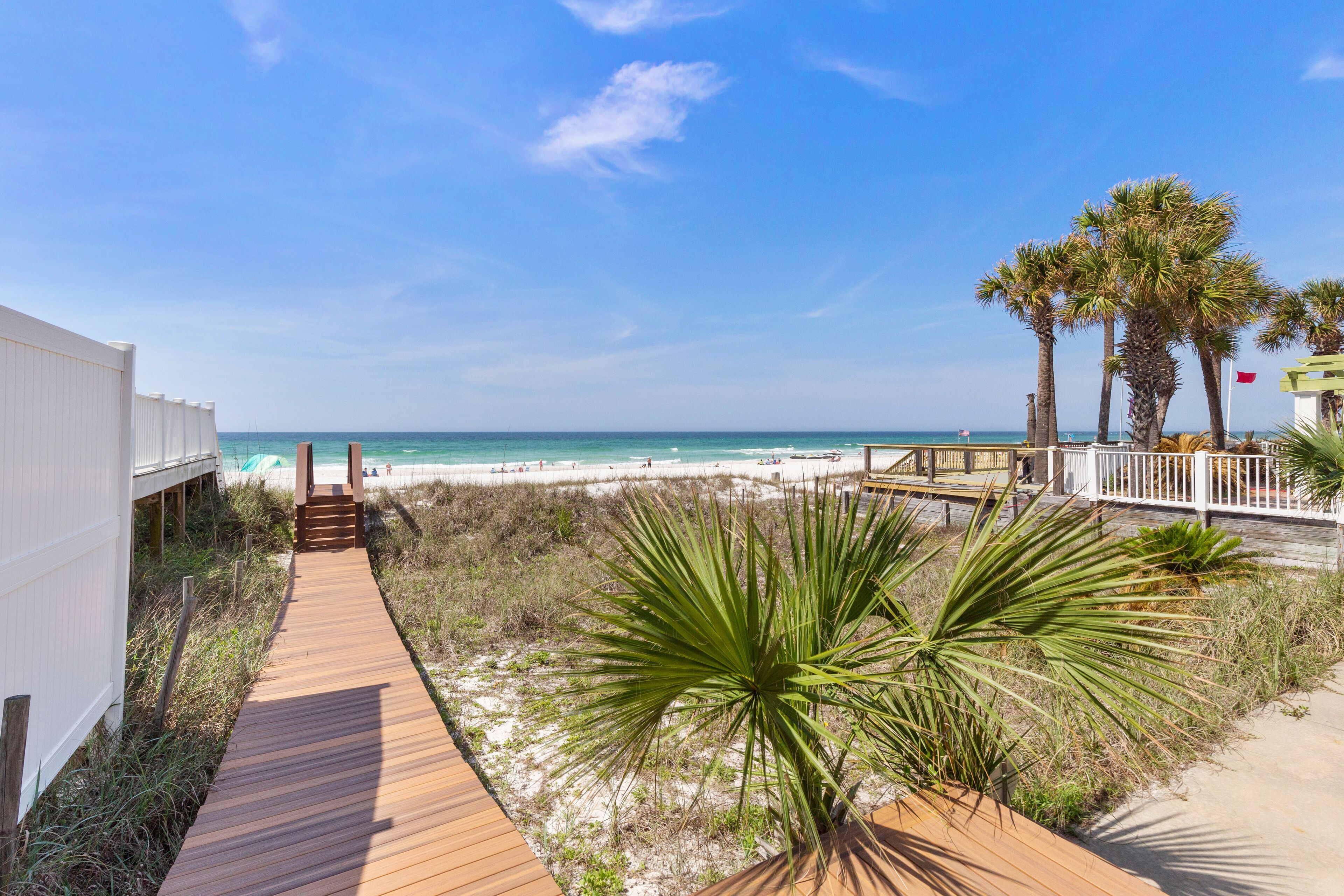 A wooden boardwalk leading to a beach with palm trees and a clear blue sky.