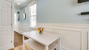 A room with a white table, a vase with flowers, a white door, and a window with blinds. - New Jersey Abode - Near Theme Parks, Walk to Beach (Keansburg)