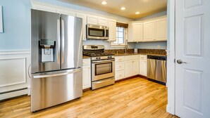 A modern kitchen with stainless steel appliances, white cabinetry, and wooden flooring. - New Jersey Abode - Near Theme Parks, Walk to Beach (Keansburg)
