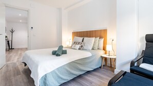 Ett modernt hotellrum med en stor säng, ett träfärgat sänggavel och ett litet nattduksbord med en lampa.