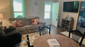 A living room with a sofa, chairs, a dining table, a TV, and a door.