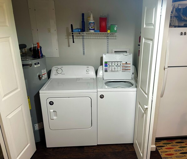 Una sala de bugaderia amb dues rentadores, una prestatgeria amb productes de neteja i un frigorífic.