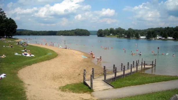 A beach with a wooden walkway leading to the water, surrounded by grassy areas and trees.