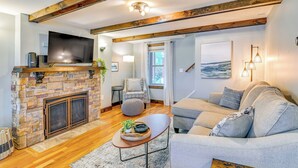 A living room with a stone fireplace, a flat-screen TV, a grey sofa, and a wooden coffee table. - Saratoga Springs Vacation Rental w/ Lake Views! (Saratoga Springs)