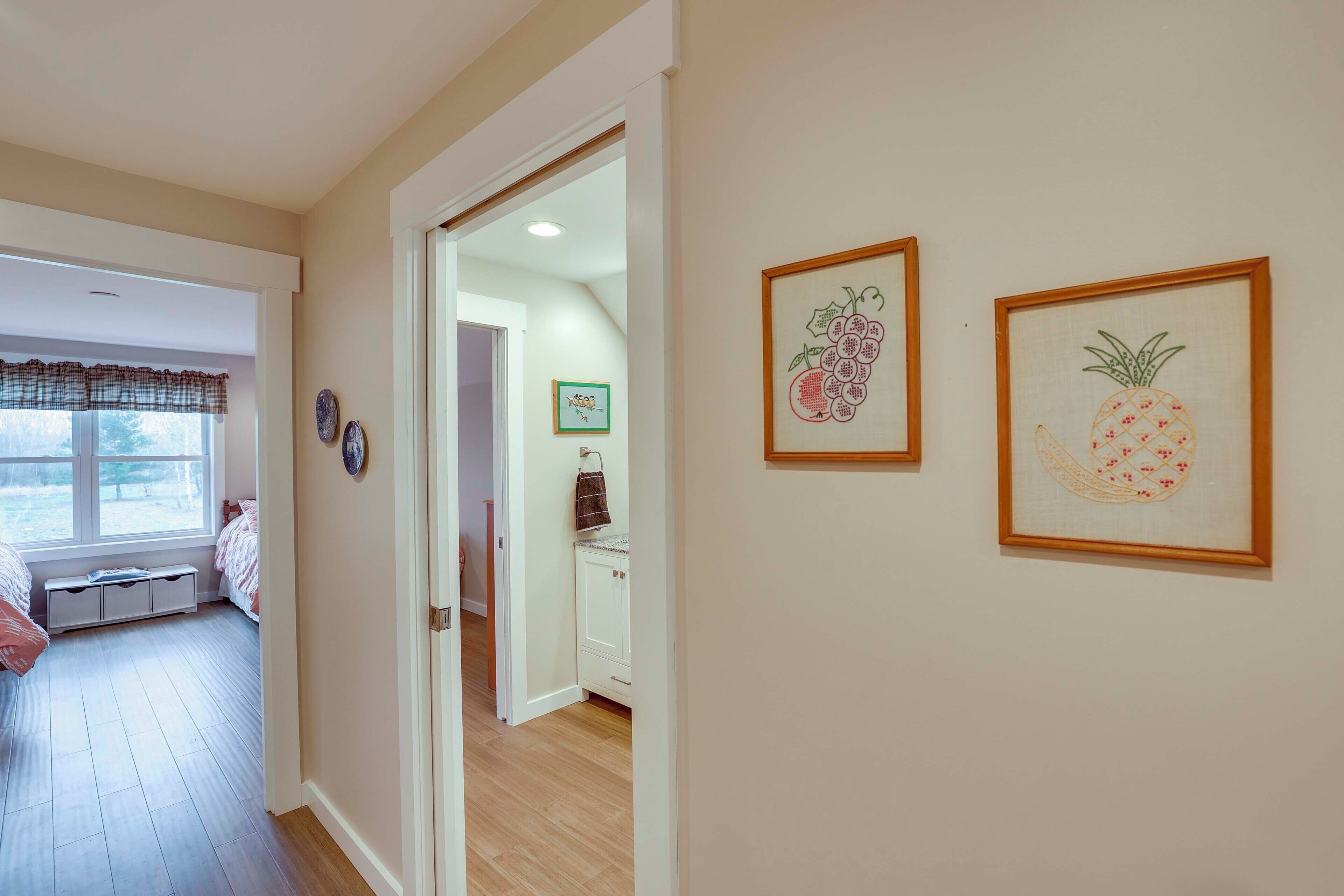 Un pasillo con una puerta que da a una habitación con ventana y un banco. Hay cuadros enmarcados en la pared.