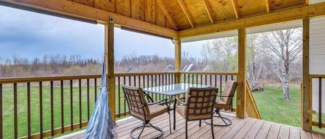 Une terrasse en bois avec une table et des chaises, un hamac et une vue sur une zone verdoyante bordée d’arbres.