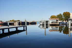 A calm waterway with boats docked, a wooden pier, and a building with a glass facade reflecting in the water. - Spreeapartment JULIA (Berlin)