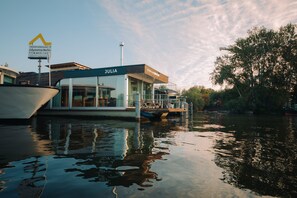 A modern floating structure named 'JULIA' with a glass facade, situated on a calm body of water, likely a river or canal. - Spreeapartment JULIA (Berlin)