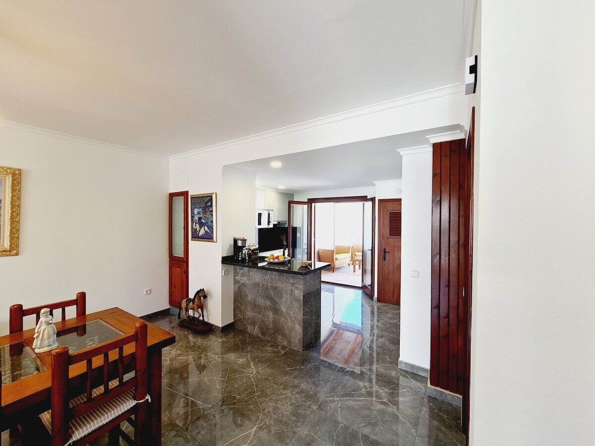 A spacious kitchen with a marble countertop and a dining area with wooden chairs.