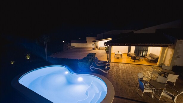 Une piscine avec des chaises longues, un espace patio aménagé avec du mobilier d’extérieur et un bâtiment doté d’un patio couvert.