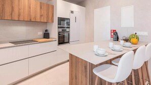 A modern kitchen with white cabinets, a wooden countertop, and a dining area with white chairs and a table set for four. - House in Sineu with excellent views of the Tramuntana (Sineu)