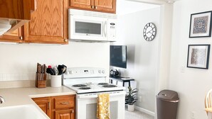 Una cucina con mobili in legno, un forno a microonde, un fornello, un lavello e una sveglia appesa al muro.