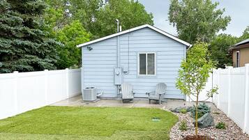 Une maison d’un seul étage, de couleur bleu clair, avec une clôture en bois peinte en blanc, une petite pelouse et deux chaises Adirondack.