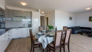 A modern kitchen with white cabinets, a dining table set for four, and a grey sofa in the living area. - Holiday apartment with large balcony and sea view (Crikvenica)