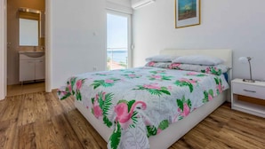 A bedroom with a bed, a nightstand, a bedside table, a window with a view, a bathroom with a sink and mirror, and a door leading to another room. - Holiday apartment with large balcony and sea view (Crikvenica)