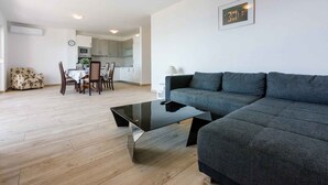 A modern living room with a grey sofa, a black glass coffee table, and a dining area with a white table and chairs. - Holiday apartment with large balcony and sea view (Crikvenica)