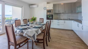 A modern kitchen with white cabinets, a dining area with a table set for six, and a view of the sea through the sliding glass door. - Holiday apartment with large balcony and sea view (Crikvenica)