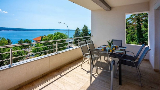 A balcony with a table and chairs, overlooking a body of water and greenery. - Holiday apartment with large balcony and sea view (Crikvenica)