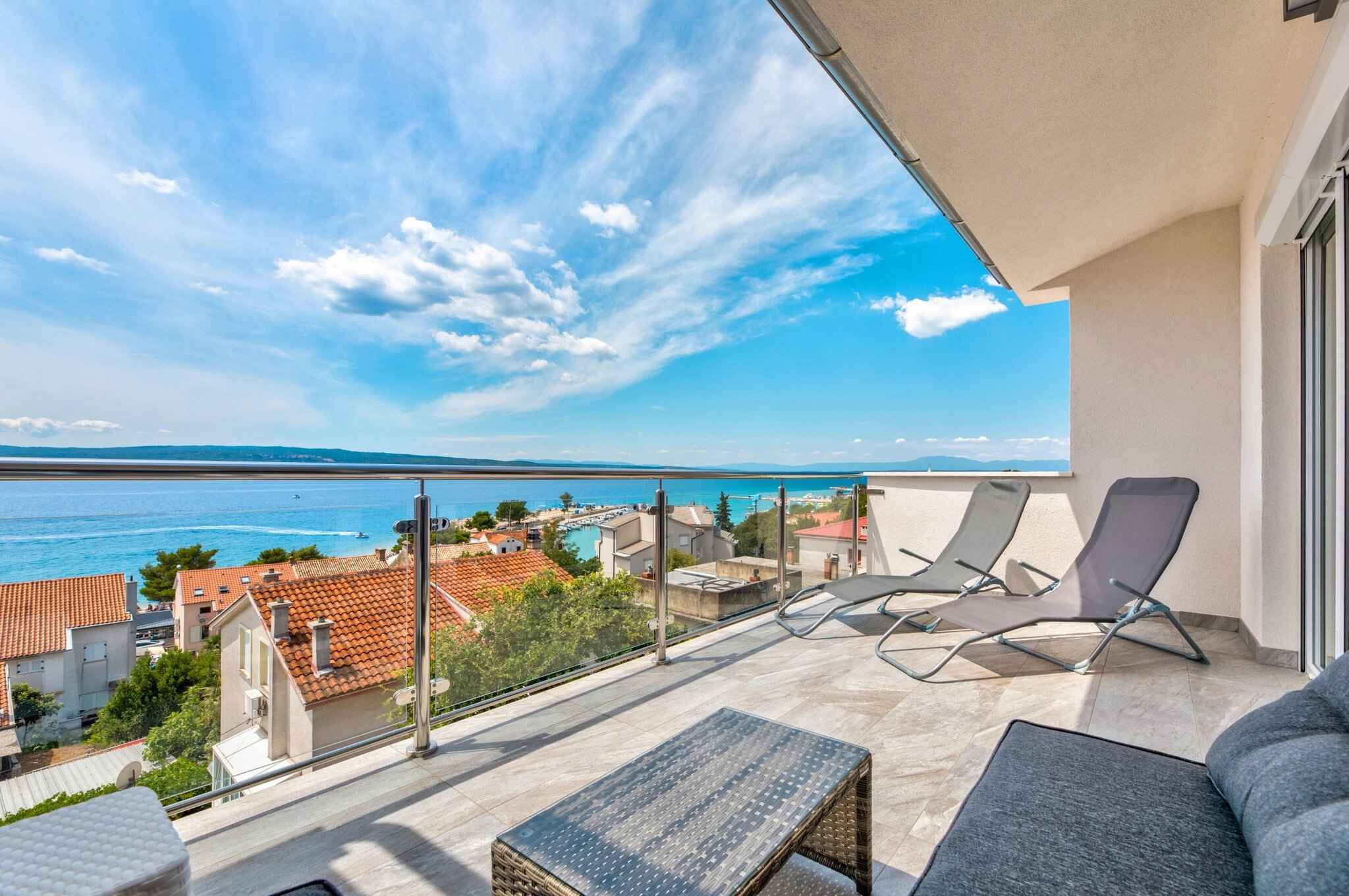 Een balkon met uitzicht op zee, twee lounge fauteuils en een kleine tafel.