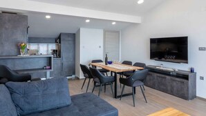 Un espace de vie moderne comprenant un coin repas, une cuisine et un grand téléviseur à écran plat fixé au mur.