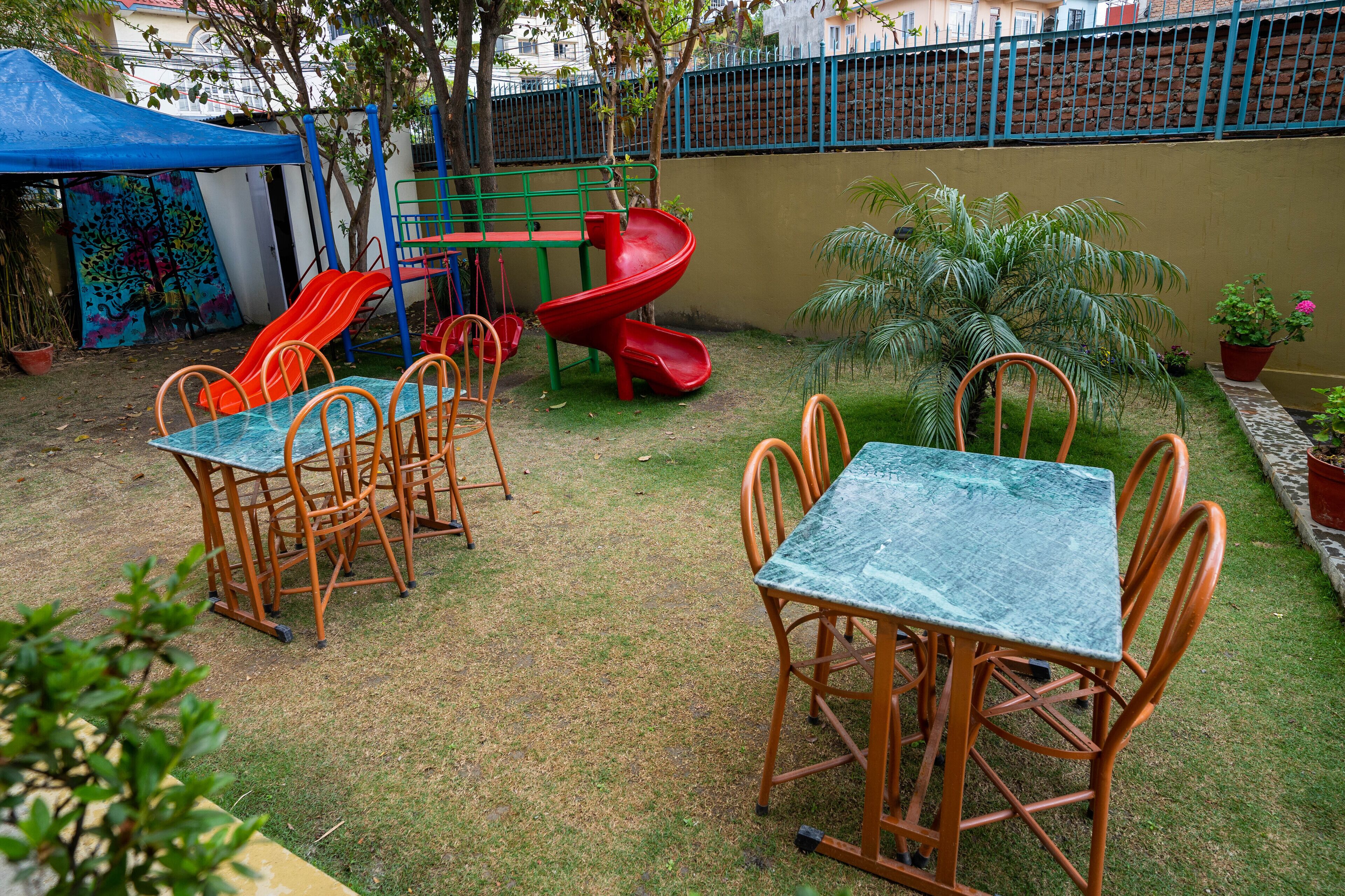Eine Terrasse mit Tisch und Stühlen, eine Rutsche und ein eingezäunter Bereich mit Baum und Topfpflanze.
