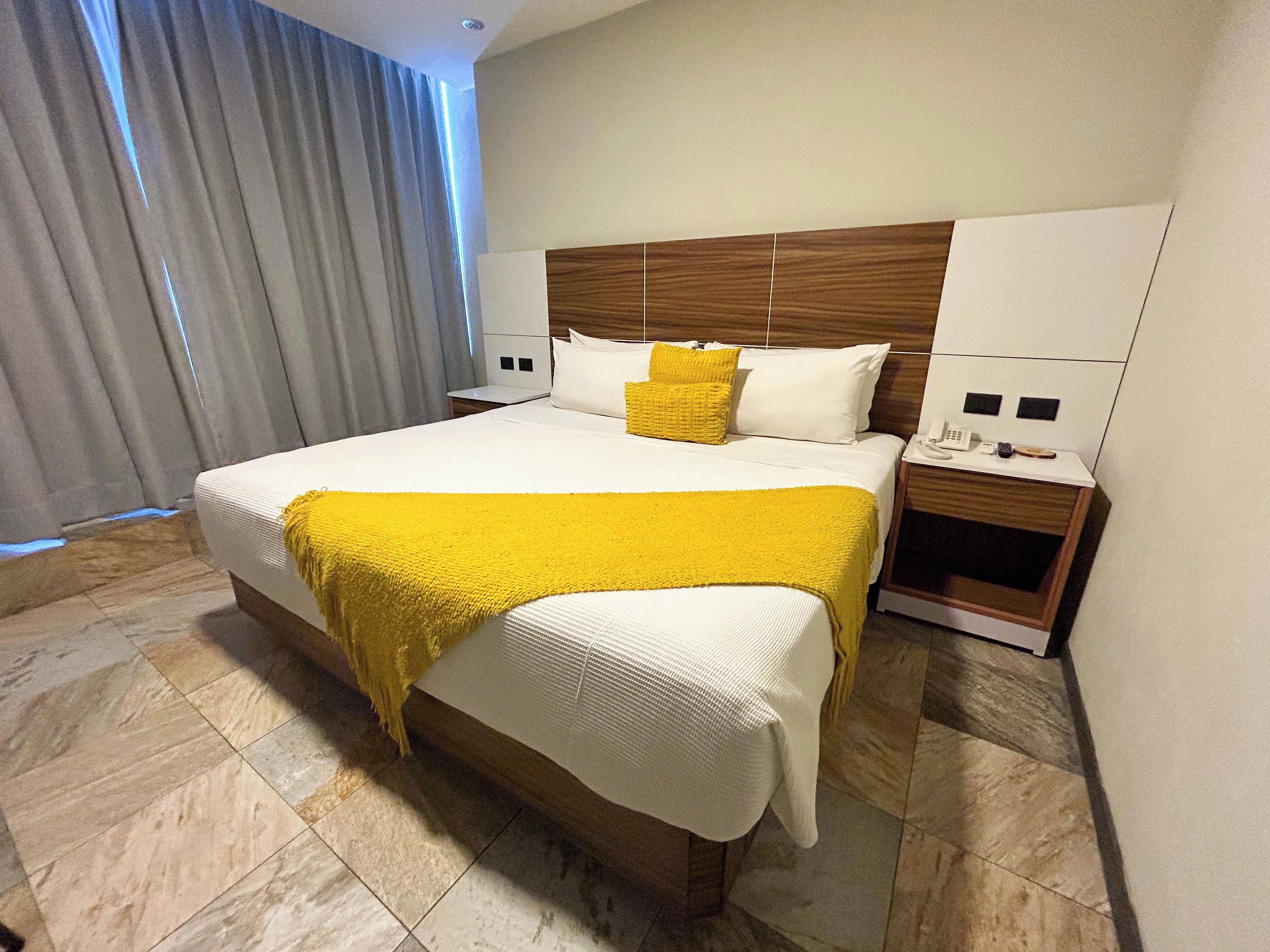 A hotel room with a large bed, a wooden headboard, two bedside tables, and a curtain.