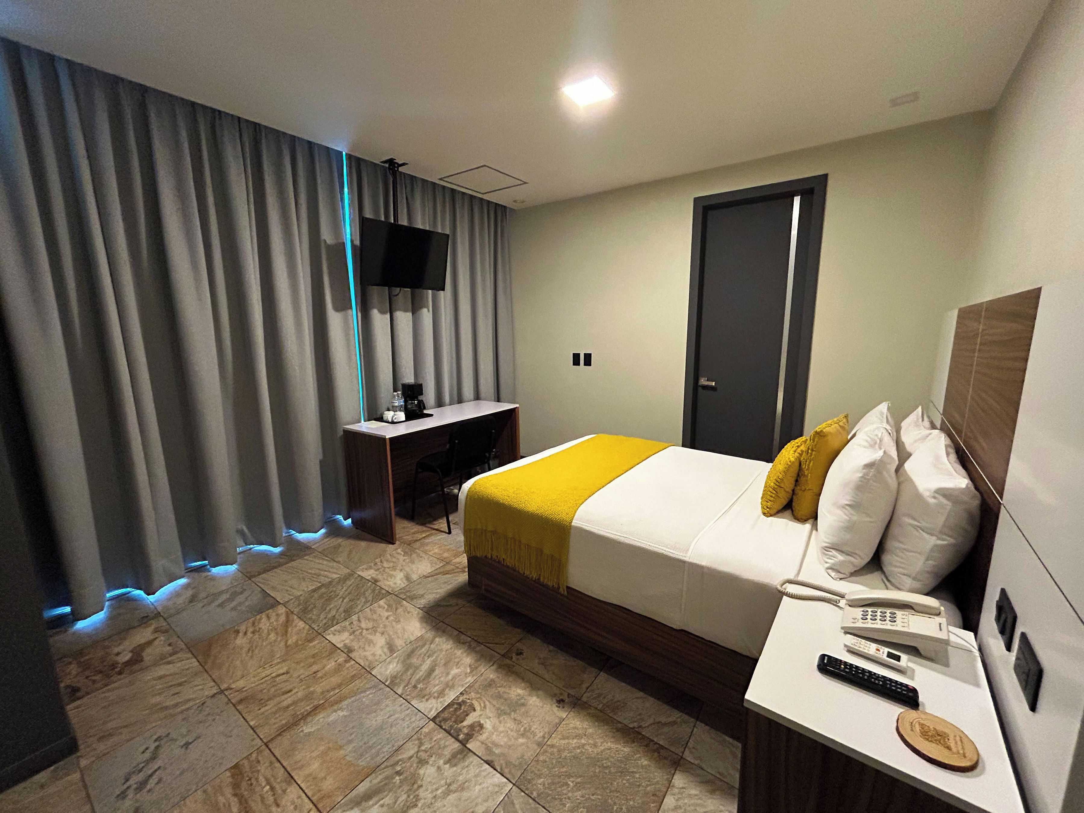 A hotel room with a bed, a desk, a TV, and a phone.