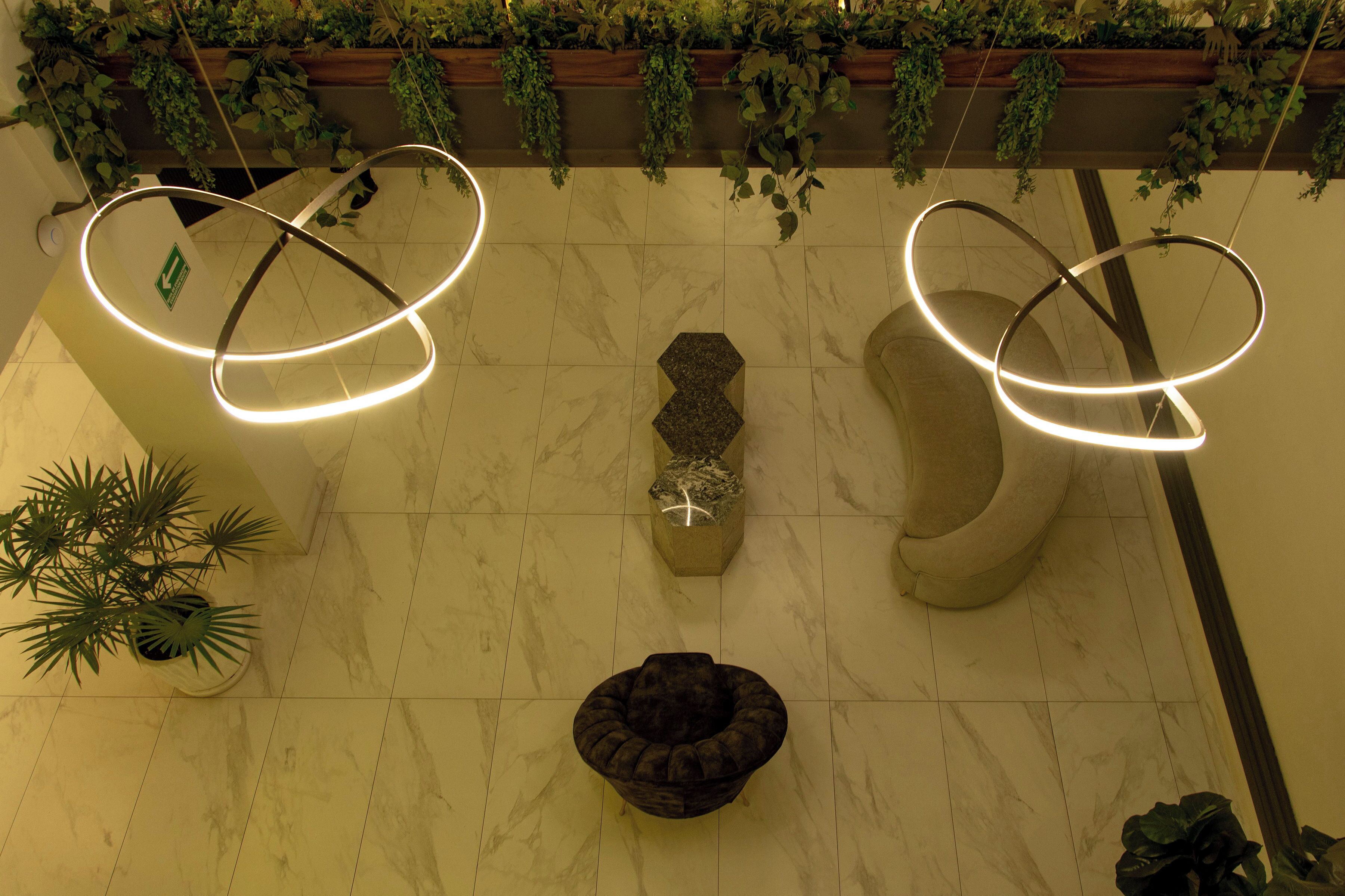 Un hall d’entrée doté d’un sol en marbre, de deux luminaires circulaires, d’un jardinier central et d’un espace détente.