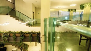 A modern lobby with a glass staircase, seating area, and indoor plants. - HVH by Yaxché (Guadalajara)