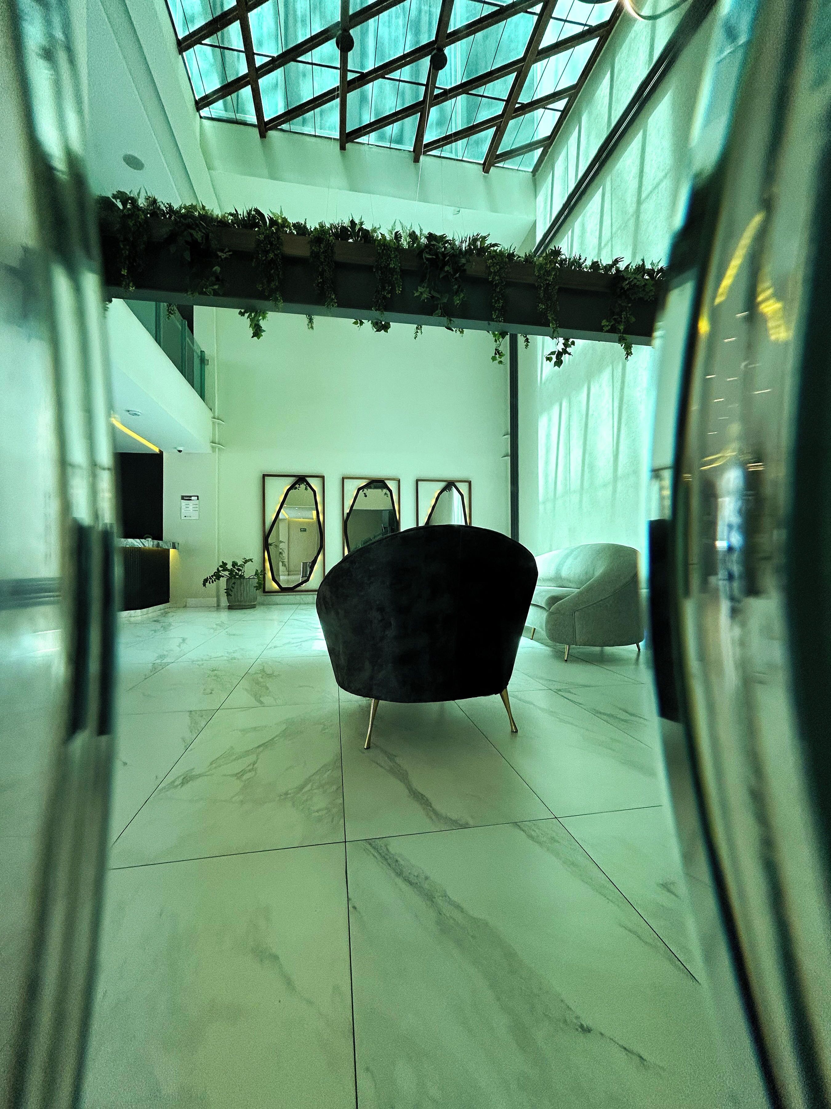 Een ruime lobby met een hoge plafond en dakraam, met een zwarte fauteuil en een grijze bank.