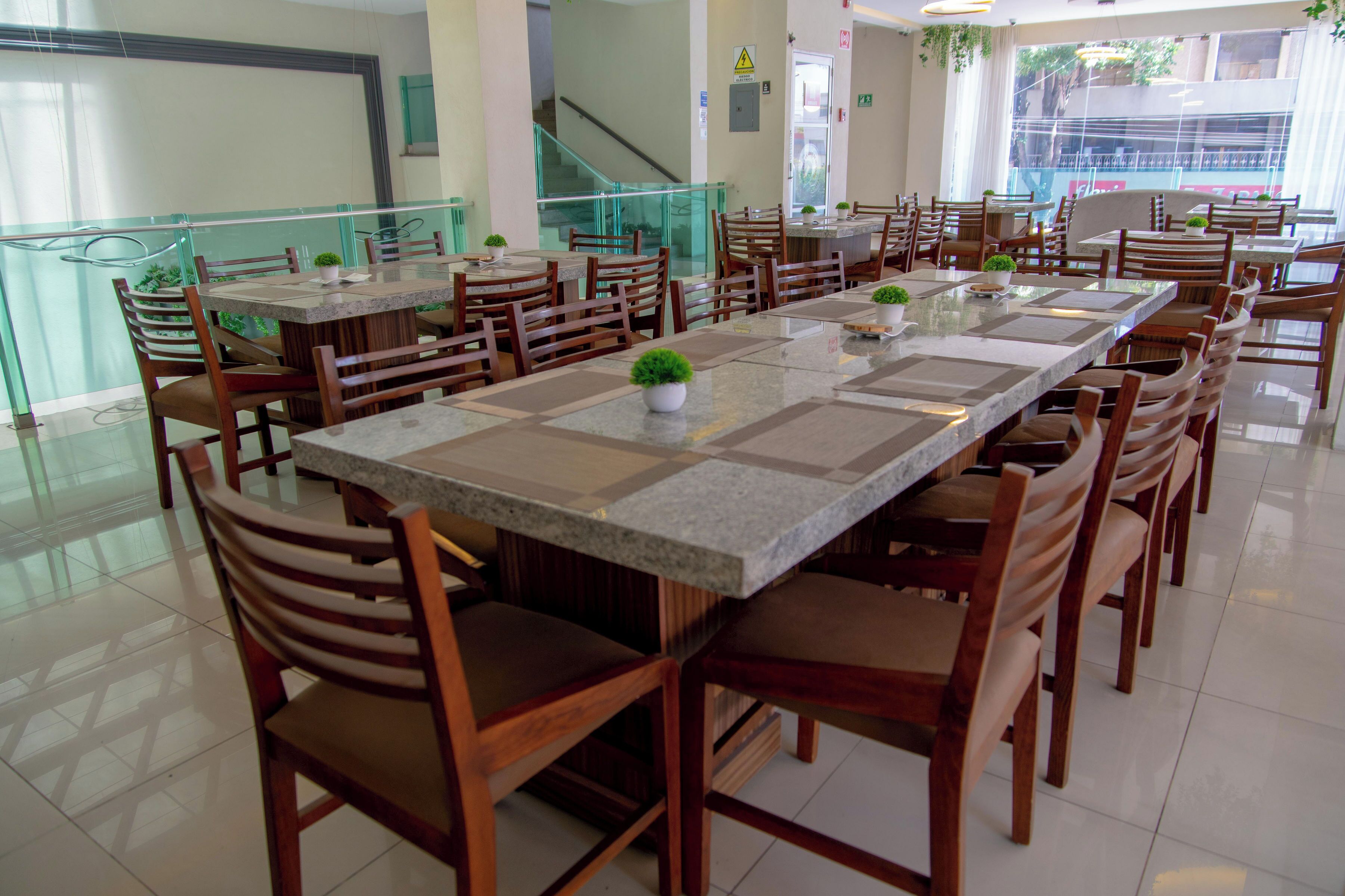 A spacious dining area with multiple tables and chairs, a staircase in the background, and a view of the outside through large windows.