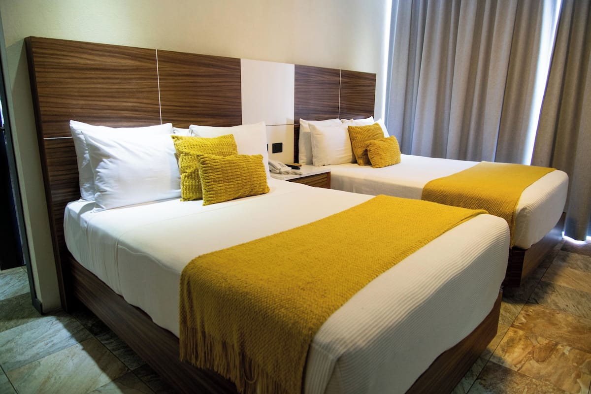 A hotel room with two beds, each with white linens and yellow throw pillows.