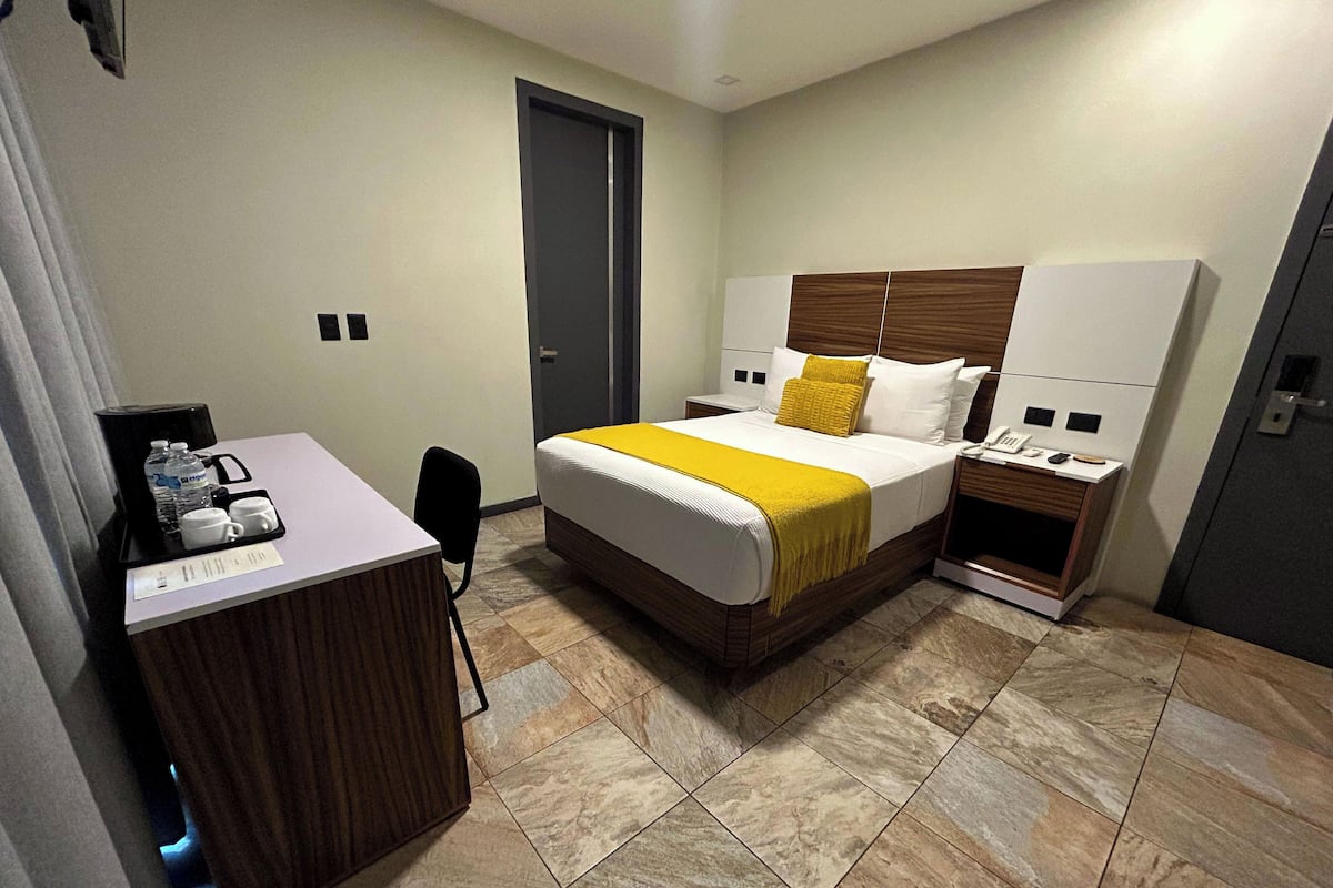 A hotel room with a bed, bedside tables, a desk with a coffee maker, and a chair.