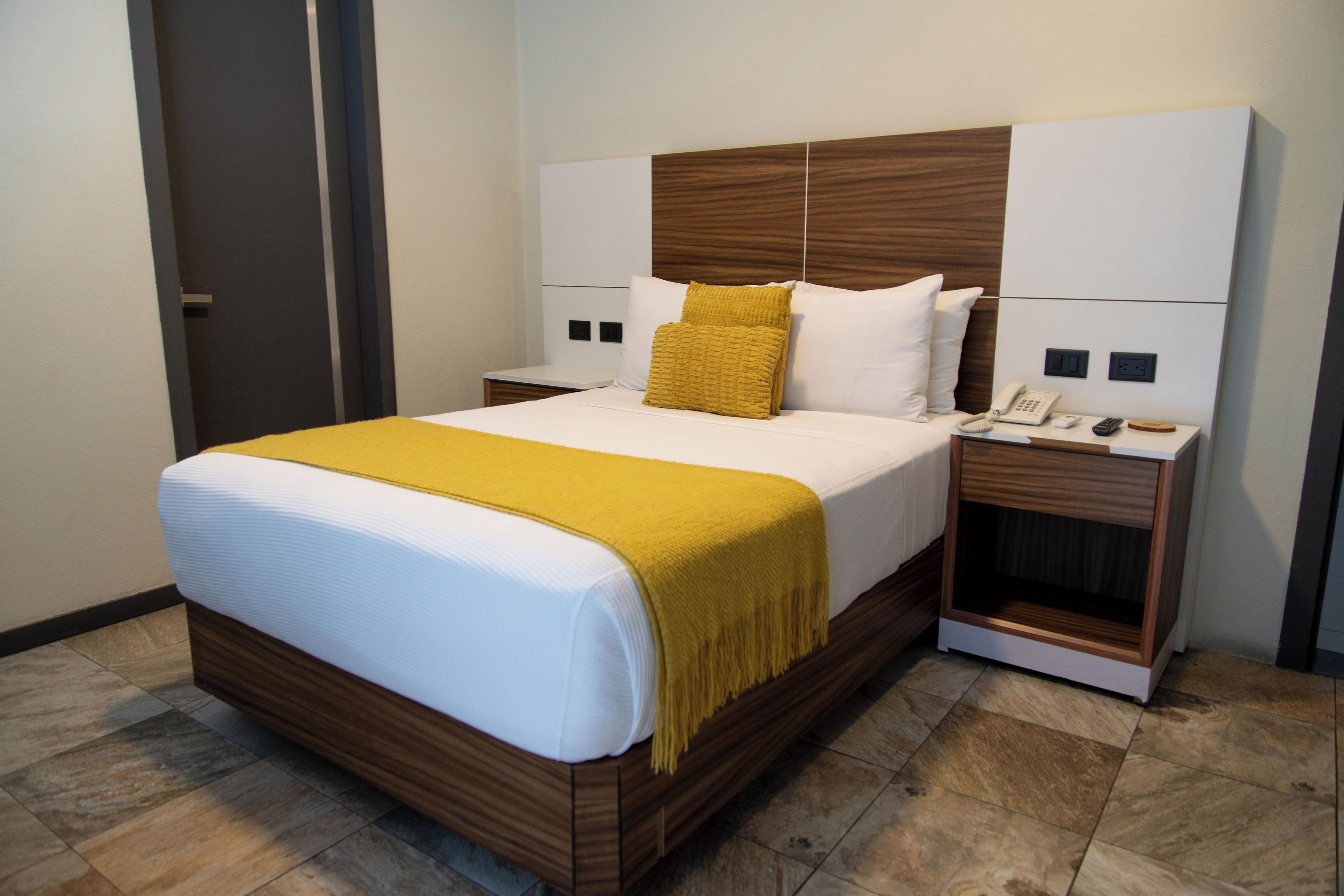 Une chambre d’hôtel moderne avec un grand lit, une tête de lit en bois, des tables de chevet avec des lampes et un téléphone.