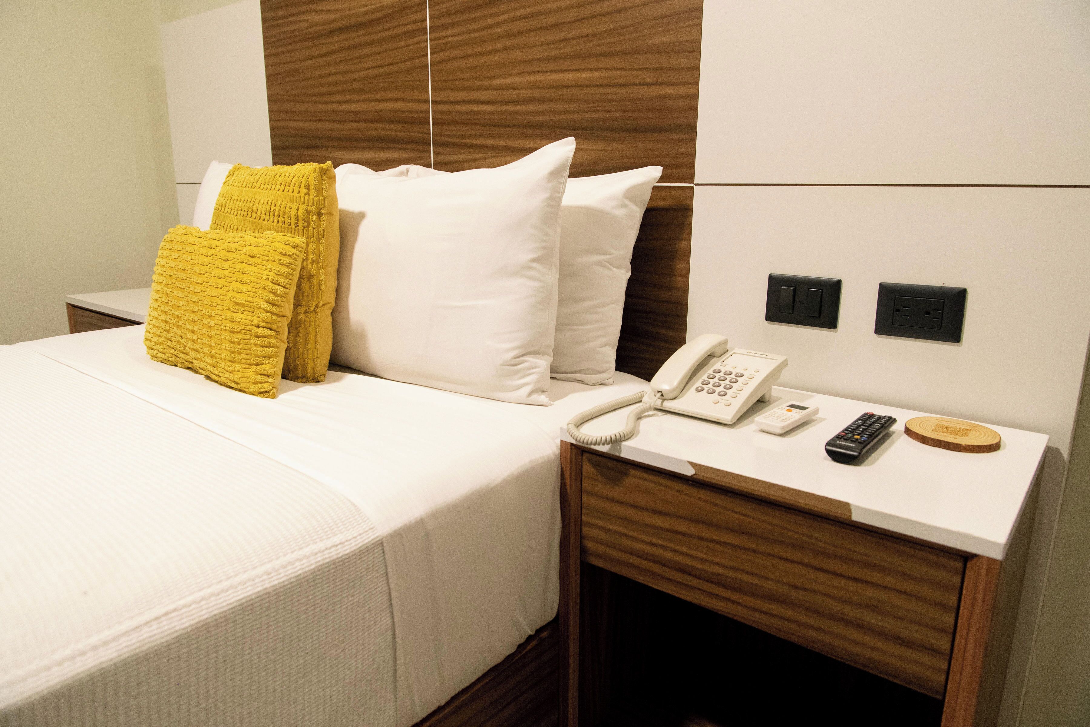 Ein Hotelzimmer mit einem Bett, einem Nachttisch mit Telefon, Fernbedienung und Steckdose.