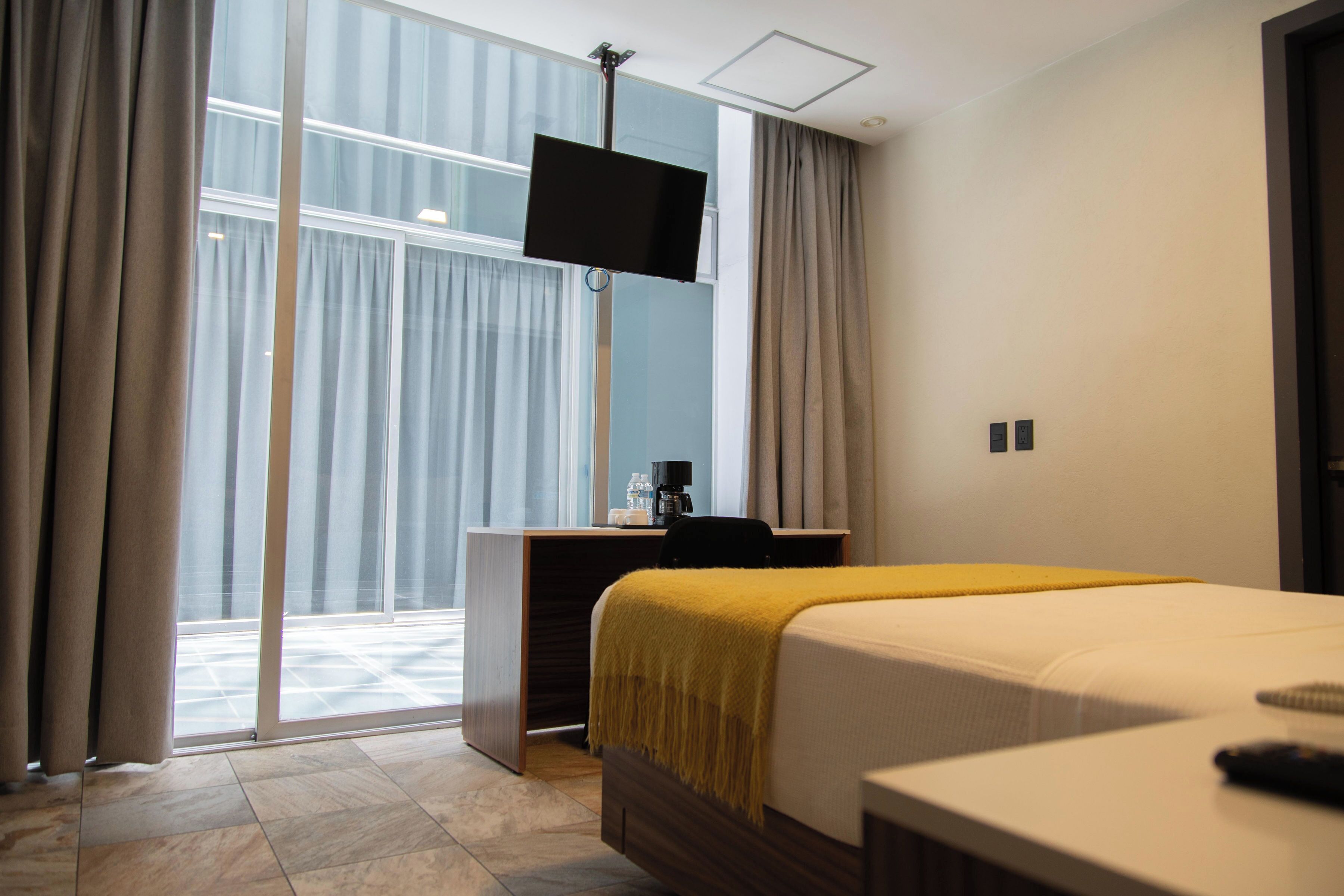 Quarto de hotel com cama, escrivaninha, televisão e vista para o exterior.