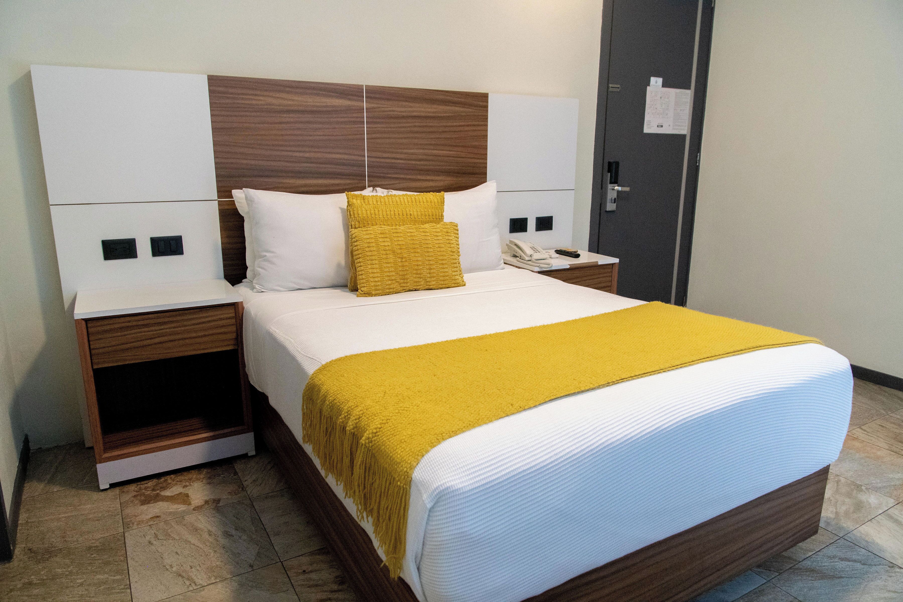 A neatly made bed with a white and yellow bedspread, a wooden headboard, and a bedside table with a telephone and a lamp.