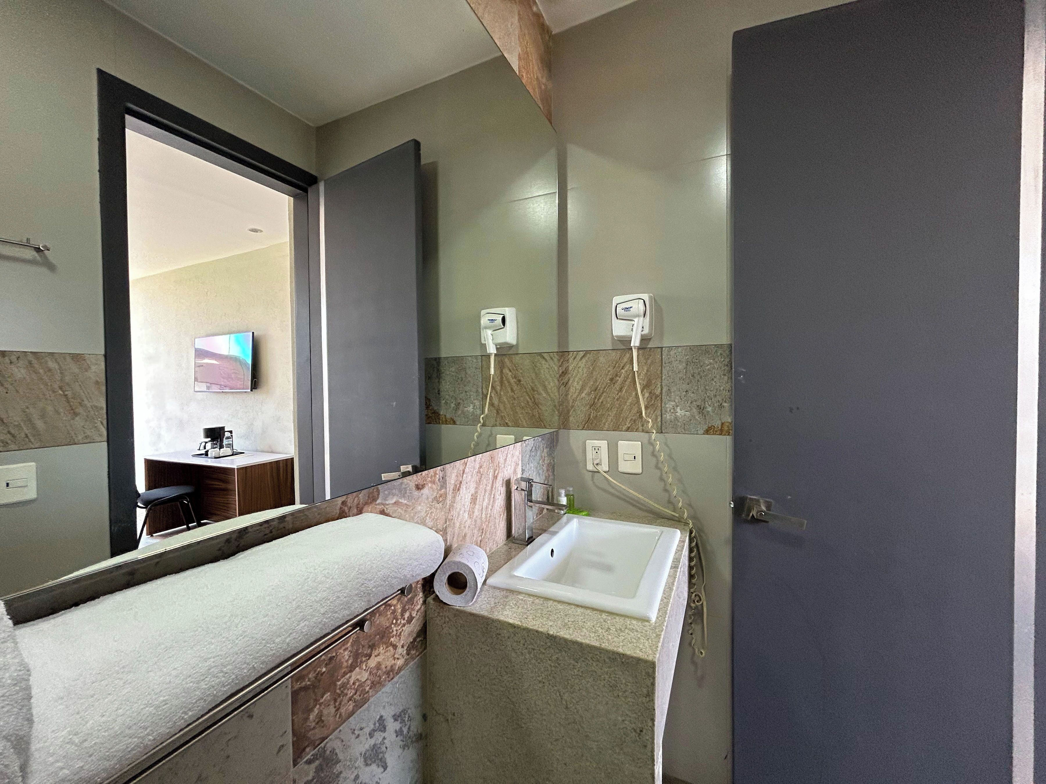 Un baño con lavamanos, espejo, toalla y secador de pelo en la pared.