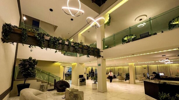 A spacious lobby with a high ceiling, a reception desk, seating areas, and a staircase. - HVH by Yaxché (Guadalajara)