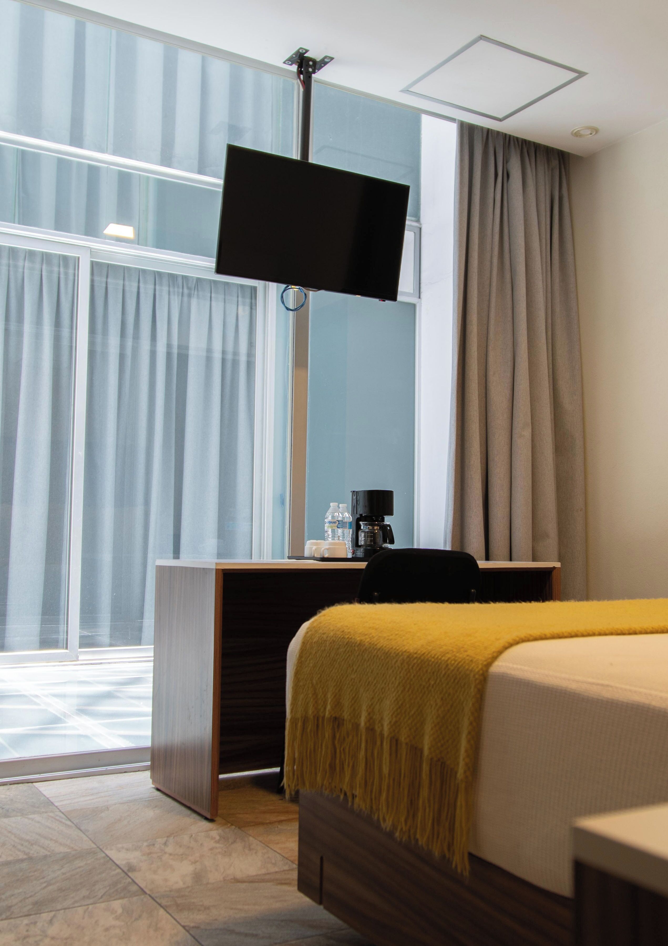 Habitación de hotel con una cama, un escritorio con computadora, televisión y ventana con cortinas.