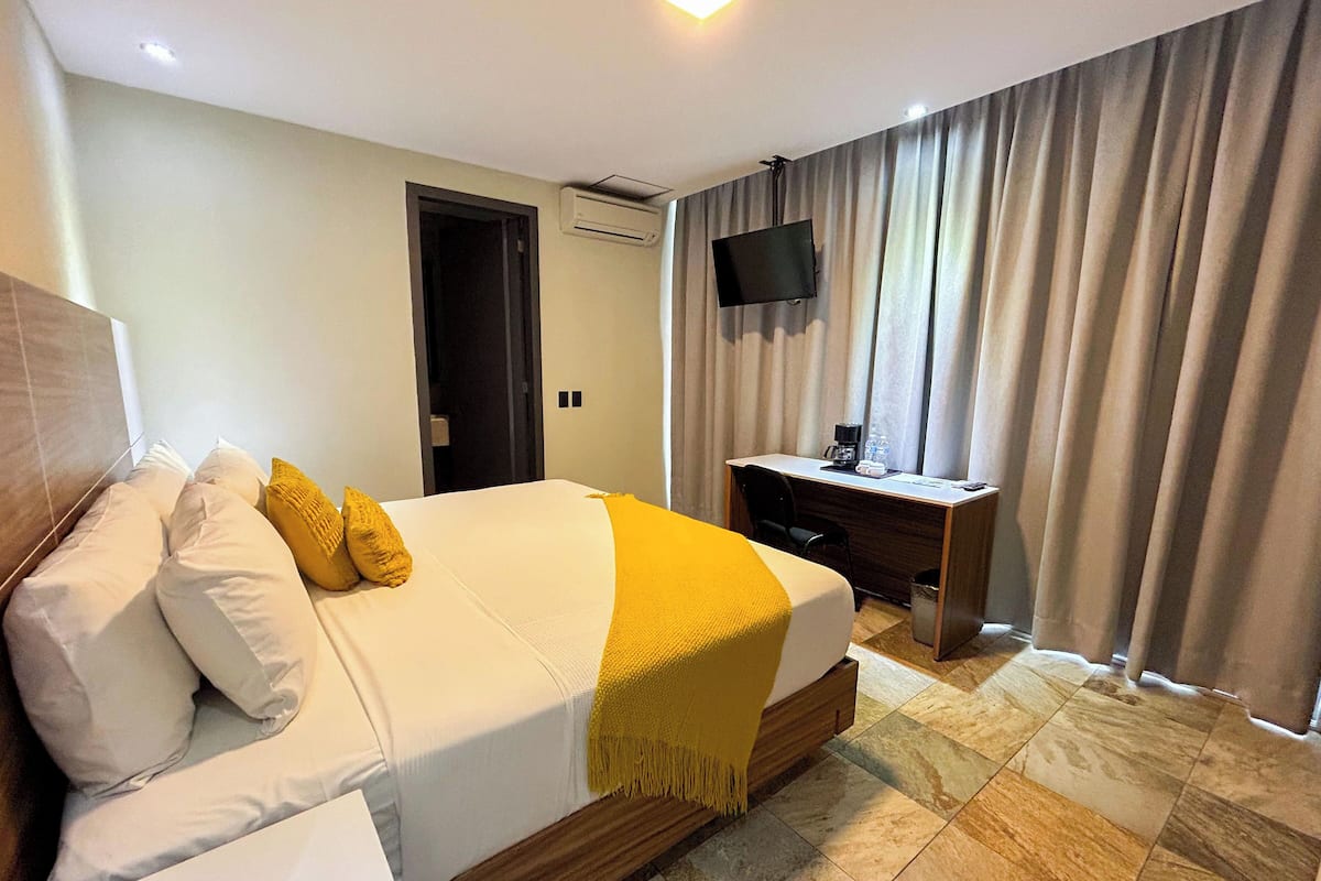 A hotel room with a bed, a desk, a TV, and a window with curtains.