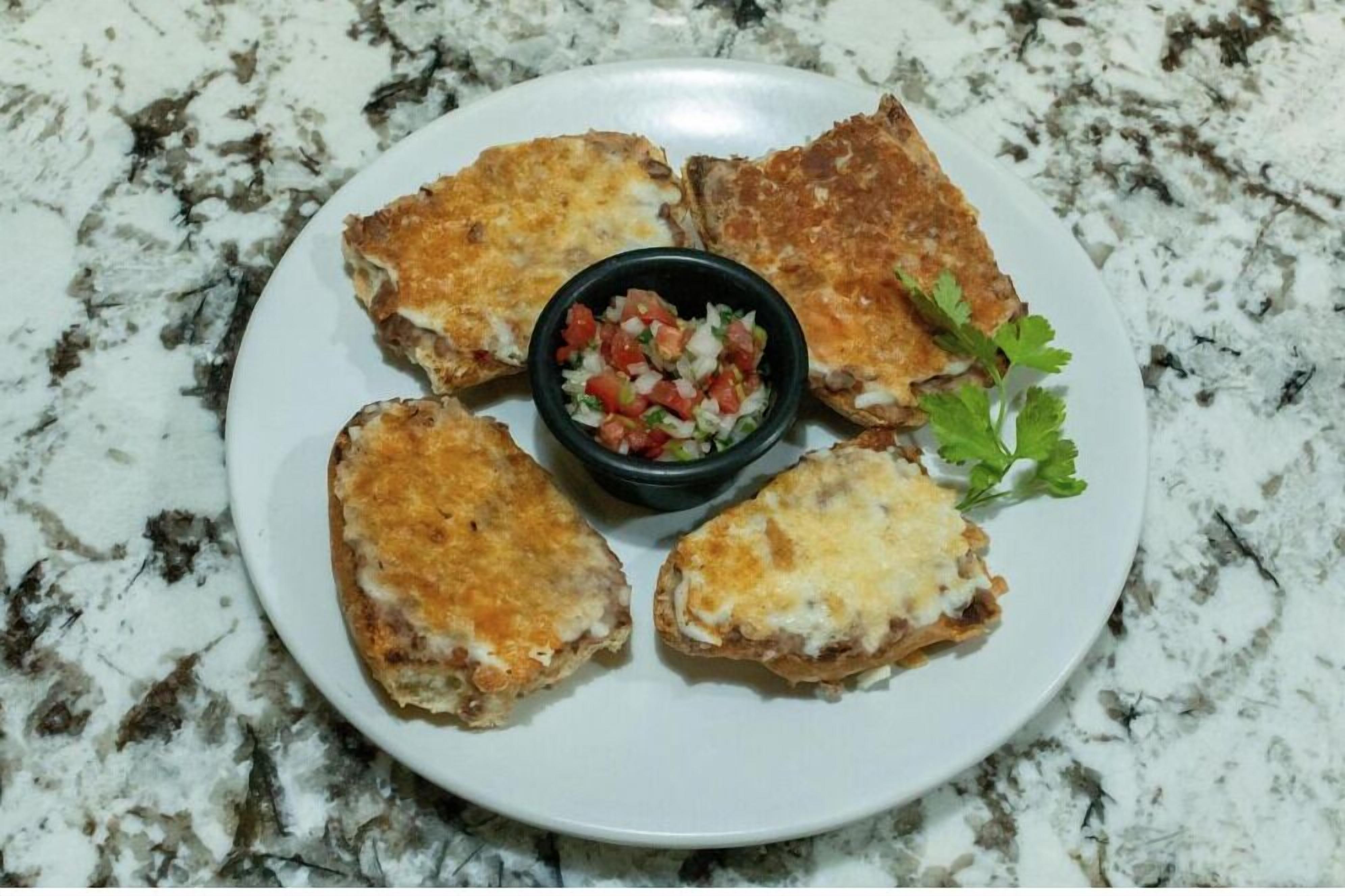 Un plato con cuatro porciones de comida y un recipiente pequeño de salsa.