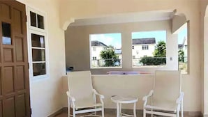 Un balcon avec deux chaises blanches et une petite table, une porte en bois, et une vue sur des maisons et de la verdure.