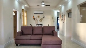 Un salon spacieux avec un grand canapé d’angle, un ventilateur de plafond et un coin repas comprenant une table et des chaises.