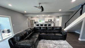 Ein modernes Wohnzimmer mit einem Ecksofa, einem Deckenventilator und einer Küche im Hintergrund.