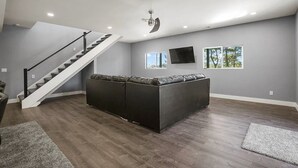 Ein großzügiger Wohnraum mit einer großen Eckcouch, einer Treppe und einem an der Wand befestigten Flachbildfernseher.