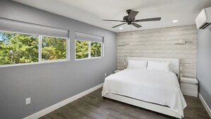 Ein Schlafzimmer mit Bett, Deckenventilator und großen Fenstern.
