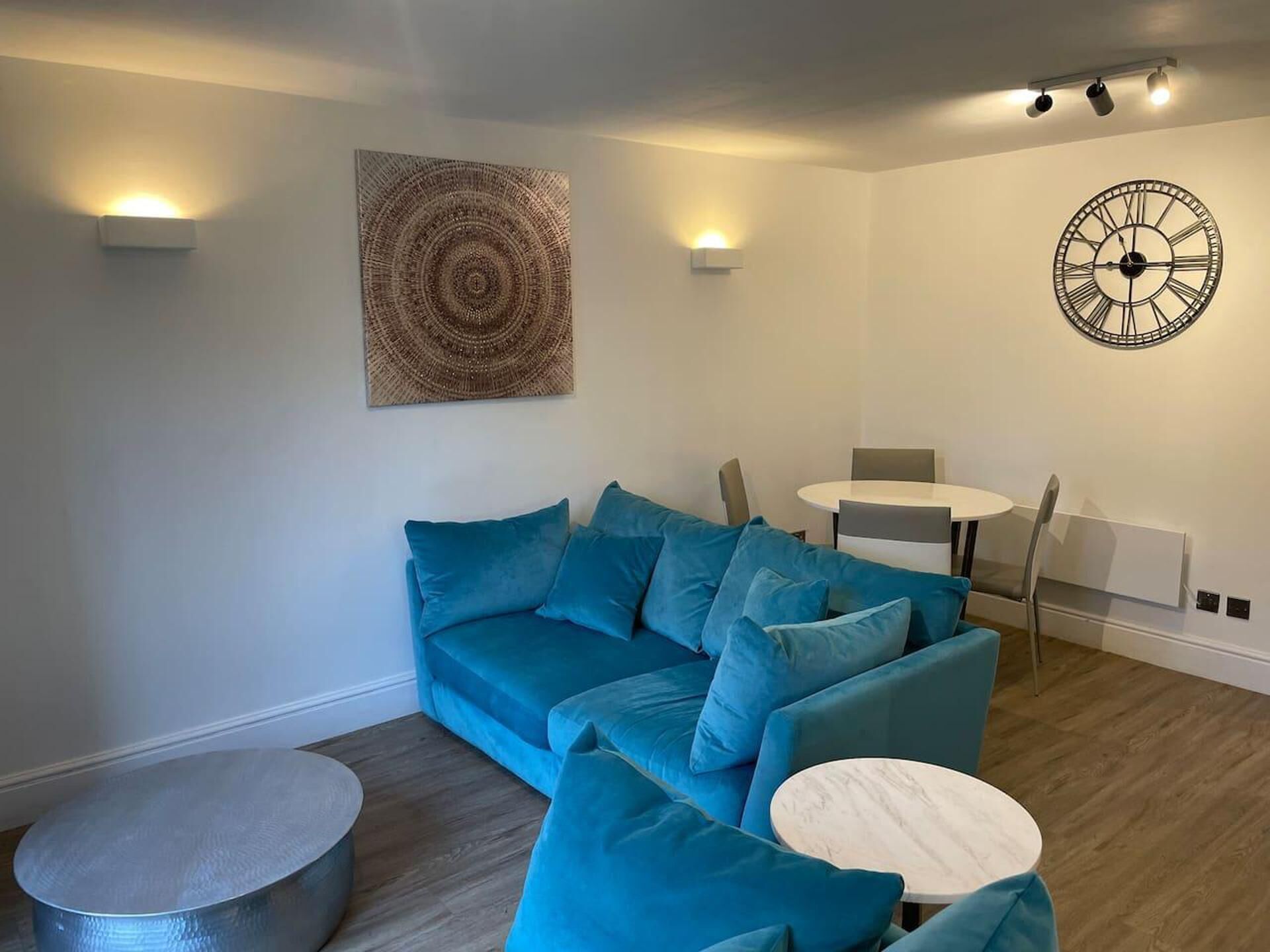 A modern living room with a blue sectional sofa, a round coffee table, and a dining area with a white table and chairs.