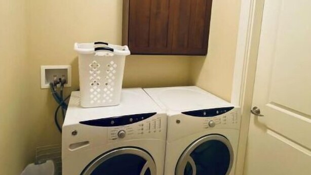 Un lavadero con dos lavadoras de carga frontal, un armario de madera arriba y una puerta a la derecha.