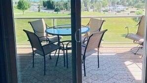 Puerta de cristal que da a un patio exterior con una mesa y sillas, con vistas a un paisaje pintoresco con montañas y una masa de agua.